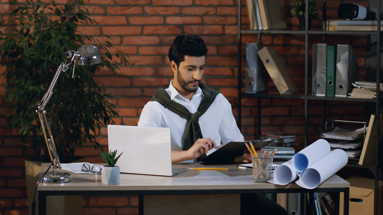 pebisnis muda arab memeriksa dan membaca beberapa dokumen atau kontrak sambil duduk di kantor di komputer