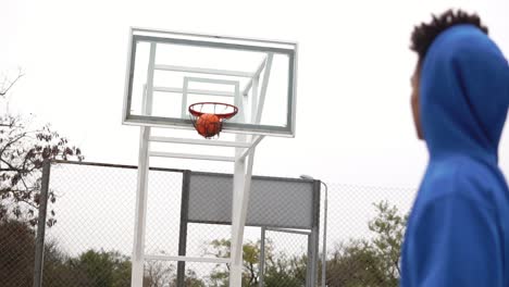 joven afroamericano jugando al baloncesto en la calle y lanzando una pelota a la canasta con éxito. disparo en cámara lenta