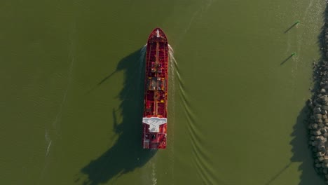 top view: a red cargo ship floats in murky green water