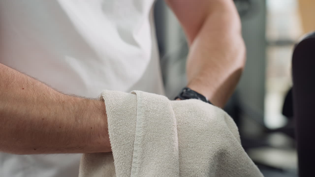 Student cleans hands with towel after intense elliptical workout showing towel texture and hand motion under natural light in modern gym recovery hygiene and self care post exercise break