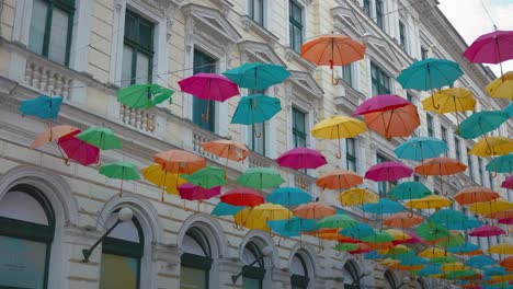 panning right shot of a bunch of colourful umbrellas placed above a pedestrian street with an old white building in the background in the city centre of timișoara