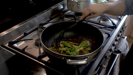 chef adding pak choi into wok and stirring it in with chilli paste