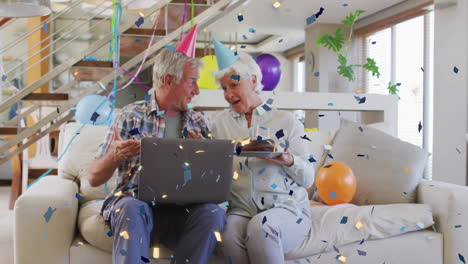 confetti animation over elderly couple celebrating birthday with cake and laptop