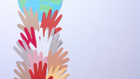 close up of hands together with globe made of colourful paper on white background with copy space