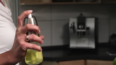 static close up shot of a woman with an oil sprayer in her hand while spraying oil for cooking in the kitchen with a coffee machine in the background