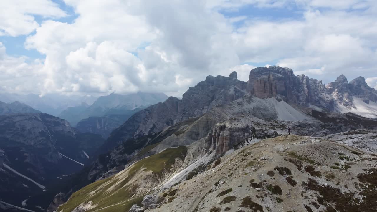 toma de drones de rotación aérea de un hombre parado en una colina de montaña con vistas a tre cime di lavaredo y el paisaje circundante después de una caminata exitosa y aventurera en los dolomitas en italia