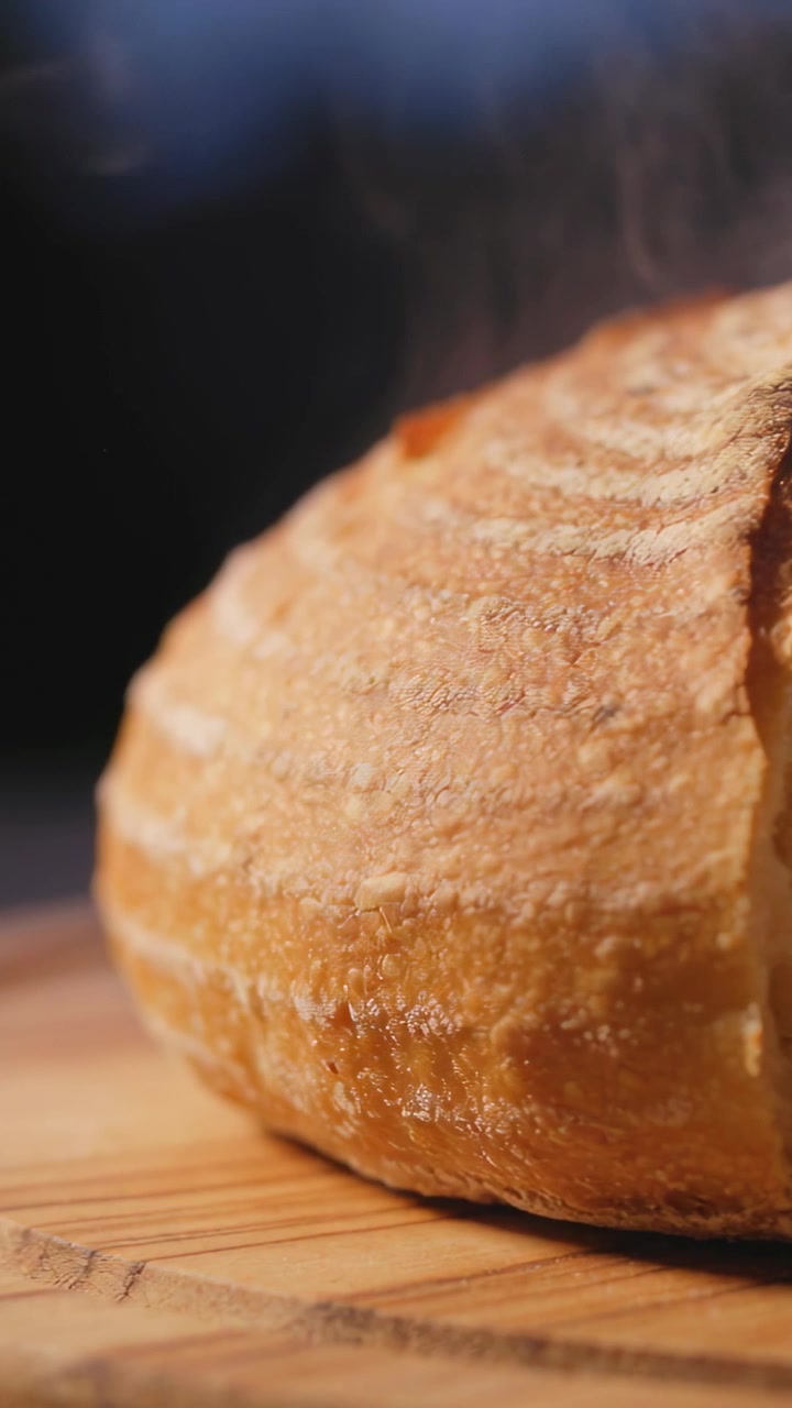 Video verticale: Pagnotta rotonda fumante che si raffredda dal forno su un tagliere in cucina, con crosta illuminata da luce calda.