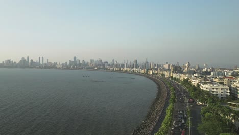 Drone-Sobrevuelo-Famoso-Paseo-Marítimo-Hacia-La-Costa-De-Mumbai,-Paisaje-Urbano-En-El-Fondo,-India