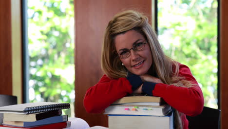 estudiante maduro sonriente sentado en el escritorio apoyado en una pila de libros