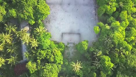 Aerial-flight-over-football-field-and-forest-on-island-in-Malaysia,-full-shot-moving-forward-in-slow-motion