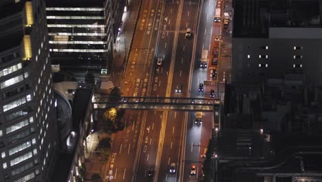 vehicles driving at the shibuya street surrounded by the high rise buildings at night in tokyo, japan