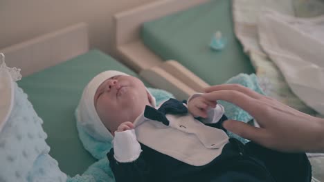 mommy puts hat on baby wearing little tuxedo at home