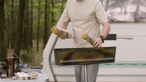 man collecting wood and putting it in a grill at the camping in the forest