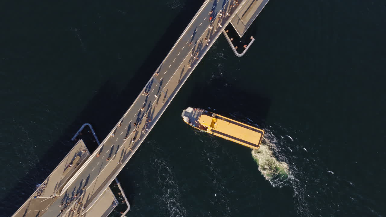 Aerial drone view of a yellow harbor bus passing under the Lille Langebro, cycling and pedestrian bridge in Copenhagen, Denmark