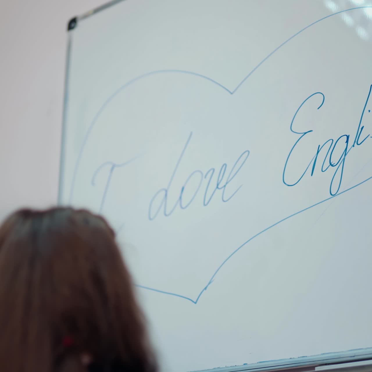 Teacher and little girl at school. Young teacher helps the pupil near the board. Female pedagogue draws the heart on a whiteboard. Back to school.