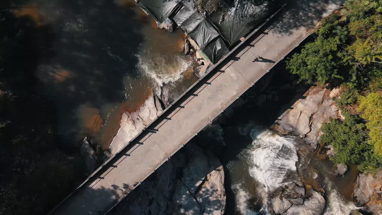 긴 그림자를 가진 사람이 화창한 날 녹색 자연 사이에서 태국의 매클랑 폭포 위의 산책로를 걷고 있습니다.