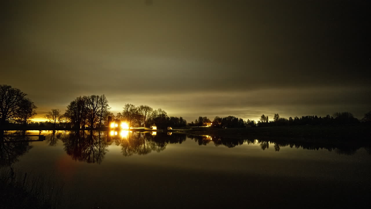 밤에 잔잔한 반사 호수 건너편에서 조명이 켜지고 꺼지는 호수 집의 타임랩스