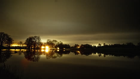 Lapso-De-Tiempo-De-La-Casa-Del-Lago-Con-Las-Luces-Encendiéndose-Y-Apagándose-Desde-El-Otro-Lado-Del-Tranquilo-Lago-Reflectante-Por-La-Noche