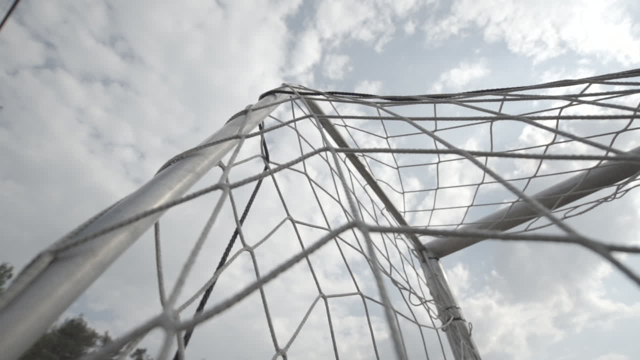 Low angle shot of the net of a football goal in slowmotion on a cloudy day LOG