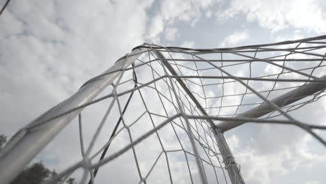 Low-angle-shot-of-the-net-of-a-football-goal-in-slowmotion-on-a-cloudy-day-LOG