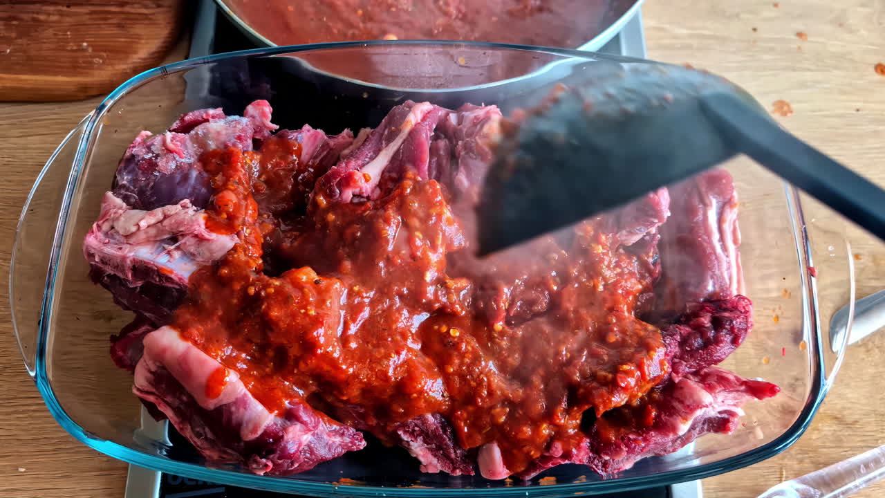 Cooking pork short ribs at home, pouring hot marinara tomato sauce over meat
