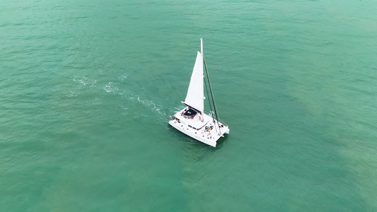 Drone captures a catamaran sailing smoothly over turquoise waters near Port Douglas, Queensland, under bright daylight