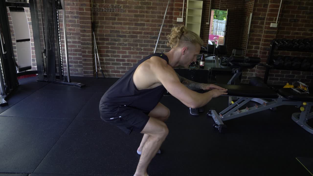 Tattoo man muscles in home gym squat to lunge
