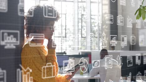 Scrolling-media-icons-over-thoughtful-biracial-casual-businesswoman-using-tablet-in-office