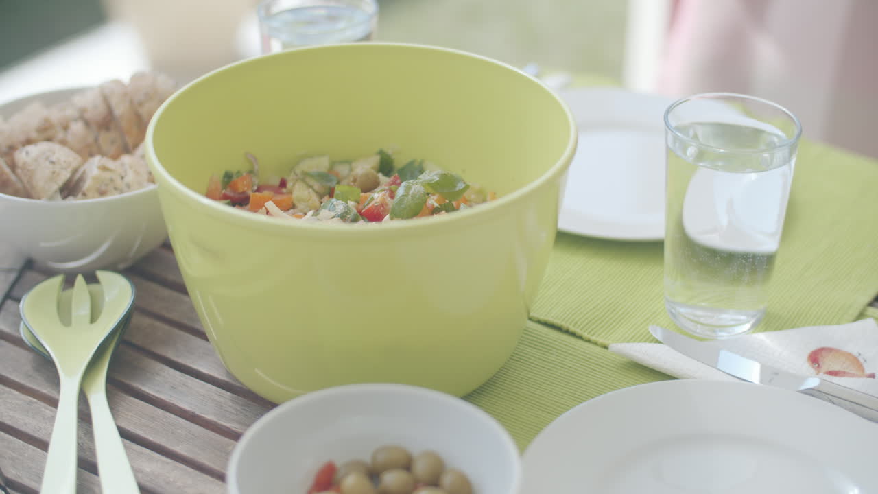 Putting bowls filled with delicious food onto a laid table on a sunny spring day. Soft commercial light. Caucasian hands putting greek salad and bread onto a wooden table