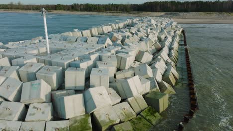 aerial establishing view of protective stone pier with concrete blocks and rocks at baltic sea coastline at liepaja, latvia, strengthening beach against coastal erosion, drone shot moving back low