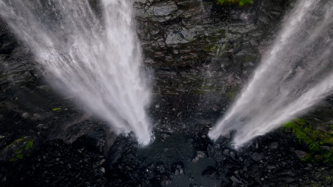A waterfall plunging from steep cliffs into black rocky terrain in the Faroe Islands