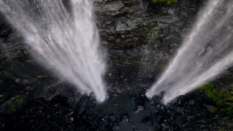 una cascada que se sumerge desde acantilados escarpados en el terreno rocoso negro en las islas feroe