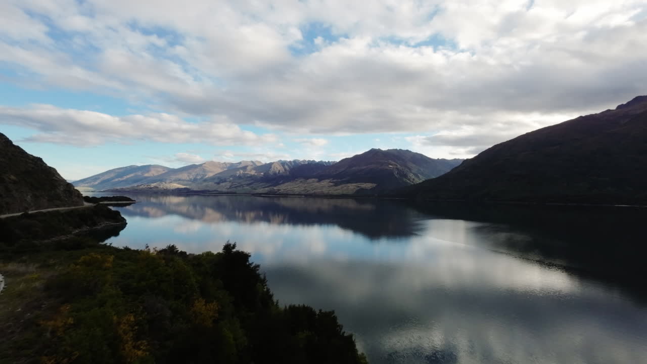 disparo aéreo siguiendo un coche conduciendo alrededor de un lago tranquilo revelando el paisaje