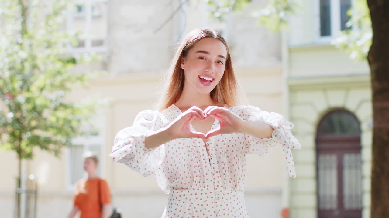 백인 여성은 사랑의 상징을 만니다. 카메라에 심장 기호를 보여주고, 만적인 감정을 표현합니다.