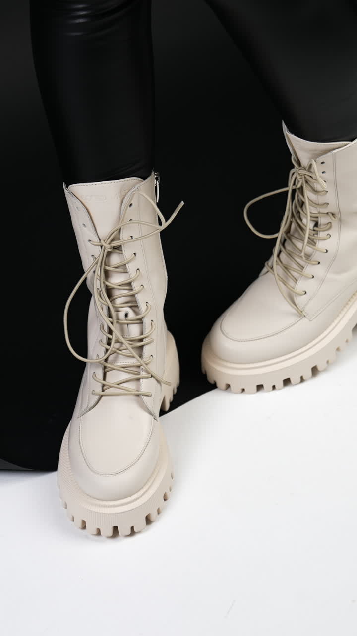 Milk-white tractor boots with laces demonstration. Female model in studio showing fashionable footwear. Vertical video