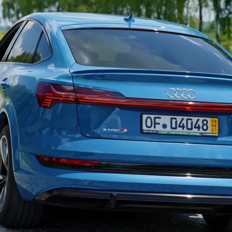 Beautiful blue audi with highlights on in daytime. E-tron luxury car model driving on a highway. Expensive electronic car on a road
