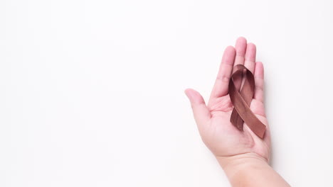 Detail-of-male-hand-holding-ribbon-in-brown-color-over-white-background