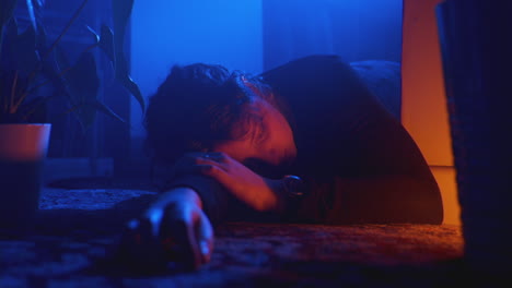 Person-sad-and-depressed-lying-down-on-floor-with-blue-room-lighting