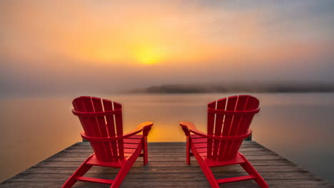 two red adirondack chairs on a misty lake at sunrise
