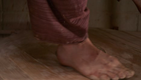 The potter rotates the wooden wheel of the potter's wheel with his feet