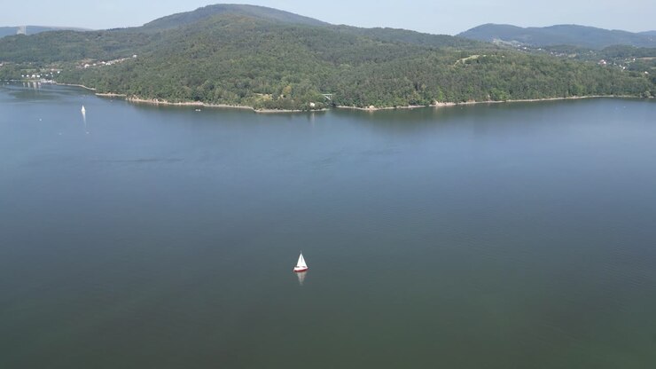 Serene lake in Beskid mountains, surrounded by greenery during a summer day - aerial view 4K