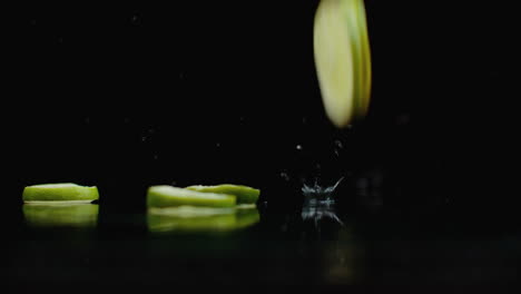 Ringe-Aus-Frischen-Grünen-Limettenscheiben-Fallen-Mit-Wasserspritzern-In-Zeitlupe-Auf-Das-Glas