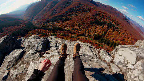 first person view of legs dangling over a mountain cliff in autumn