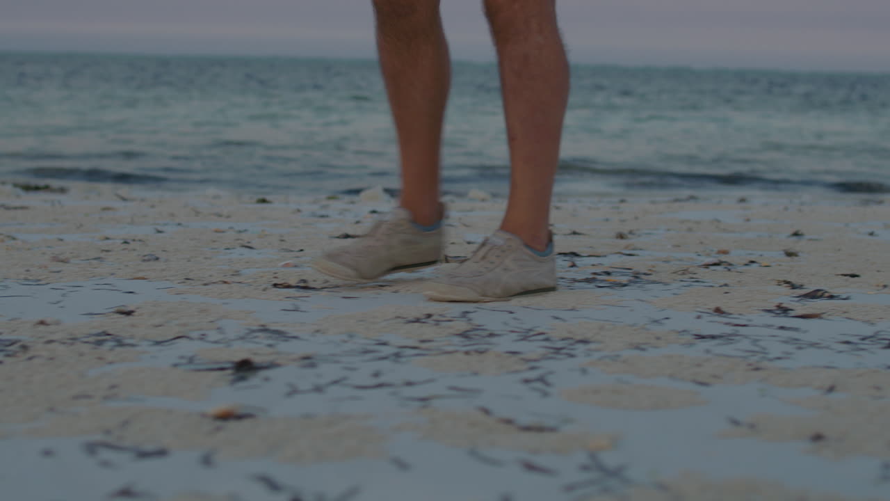 Close up on feet of man walking along the remote tropical beach during twilight.