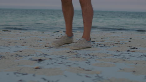 close up on feet of man walking along the remote tropical beach during twilight.