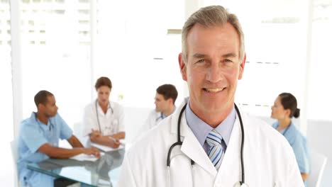 Happy-doctor-looking-at-camera-and-his-staff-behind-him