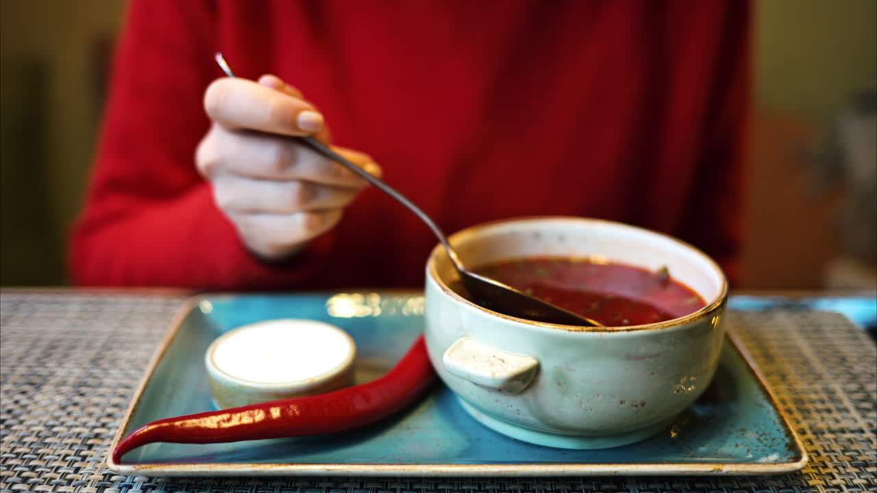 Woman eating red borscht vegetable soup in restaurant. Sour cream and red hot pepper