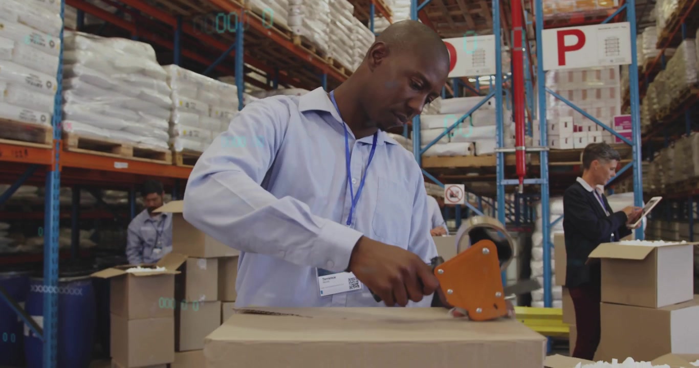 Operatore che prende un dispenser di nastro adesivo e sigilla un cartone per la logistica mentre il team consulta un tablet