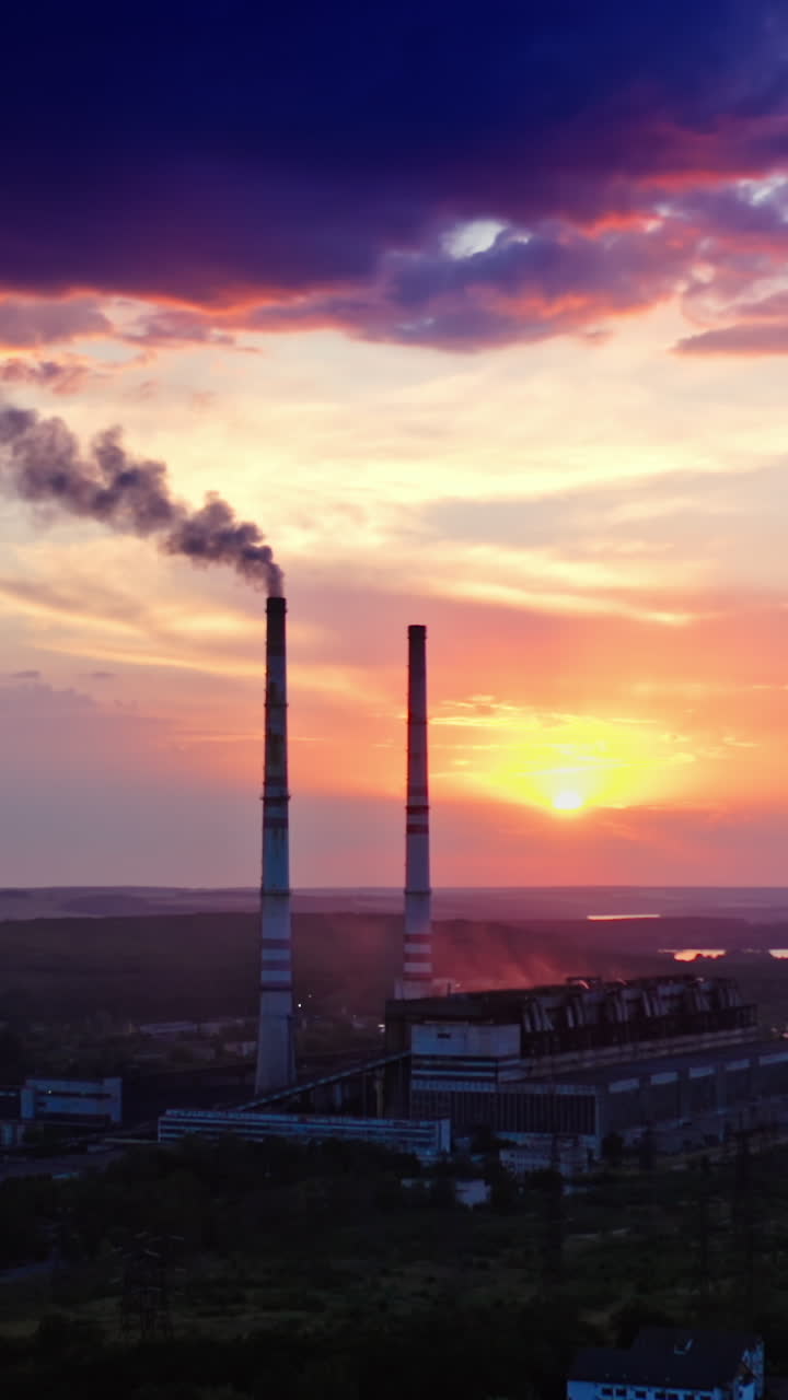 Industry pollutes nature. Chemical plant near the river in the countryside at sunset. Smoke from industrial pipe released in the air in the evening. Vertical video