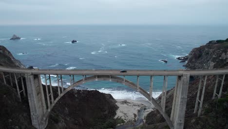 Vehicles-along-epic-Bixby-Creek-Bridge-with-Pacific-Coastline,-Big-Sur,-California,-4K-drone-shot